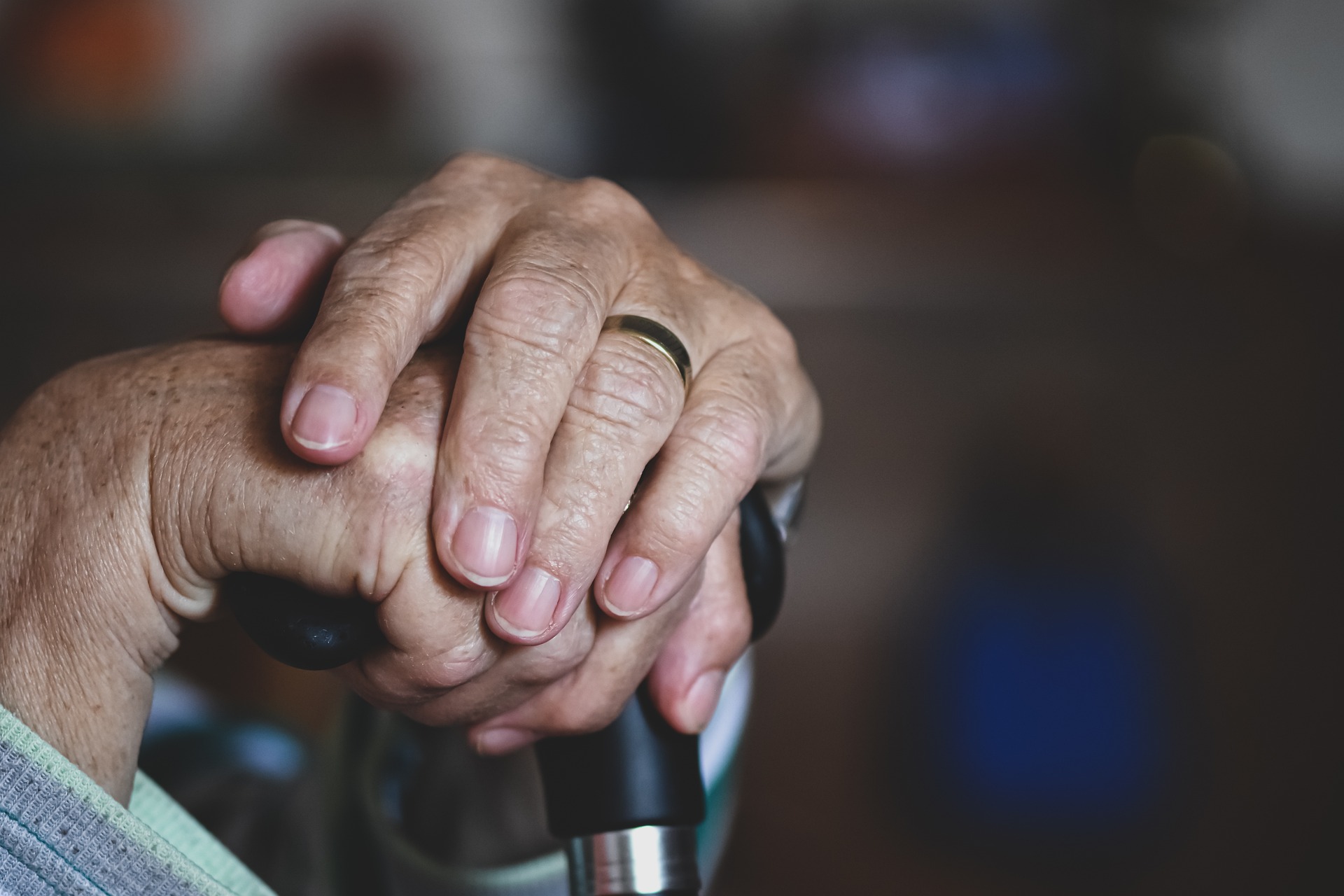 A close-up on the hands of an elderly person. The hands are on a cane.
