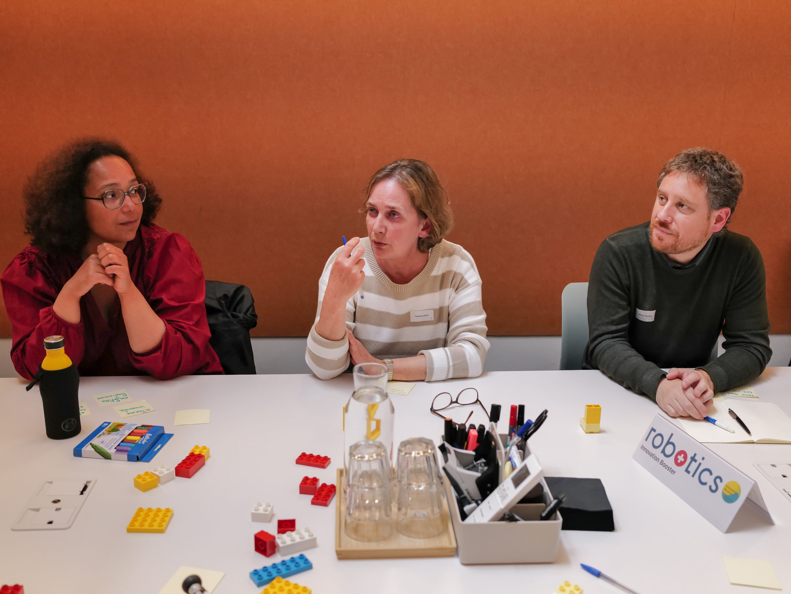 Zwei Teilnehmer/innen hören einer dritten Teilnehmerin zu, die während des Ideenfindungsworkshops spricht.